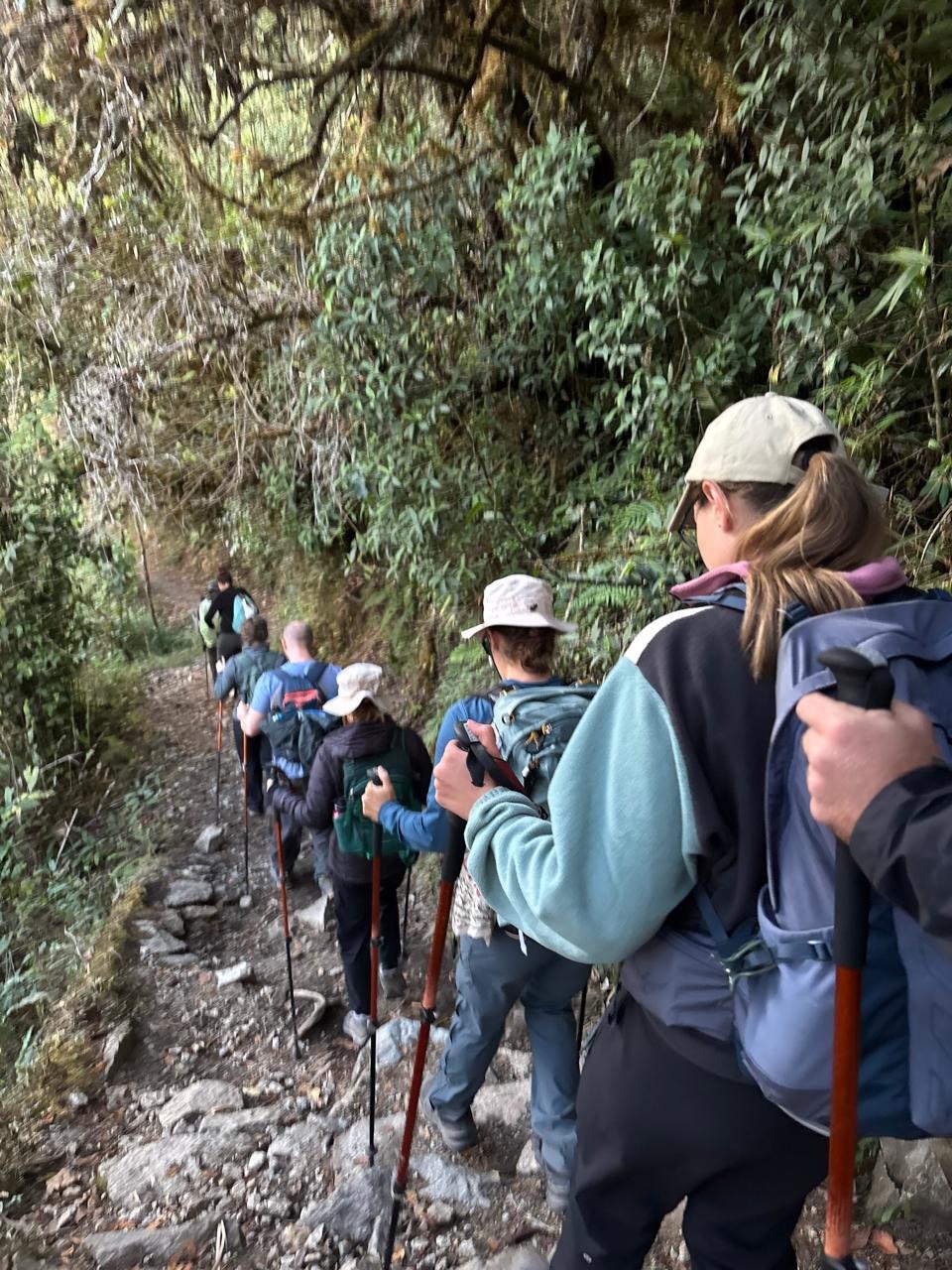 Excursionistas avanzando por el sendero inca de piedra junto a terrazas agrícolas andinas